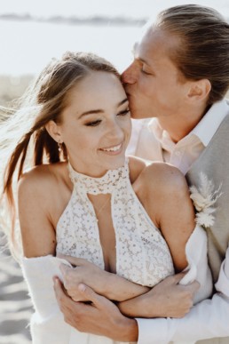 Braut und Bräutigam küssen sich mit Anstecker in Naturtönen von Ganz Unverblümt