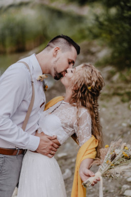 Bräutigam und Braut küssen sich mit natürlichem Brautstrauß von Ganz Unverblümt