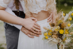 Braut und Bräutigam umarmen sich mit natürlichem gelben Brautstrauß von Ganz Unverblümt