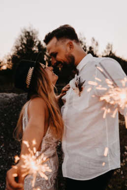 Bräutigam und Braut mit Feuerwerfern lachen sich glücklich an