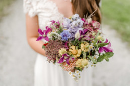Braut hält bunten Wiesenblumenstrauß von Ganz Unverblümt in die Kamera