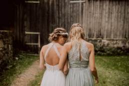 Braut und Brautjungfer mit Haarschmuck von Ganz Unverblümt stehen vor Scheune