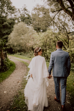 Brautpaar spaziert Weg entlang mit Brautstauß von Ganz Unverblümt