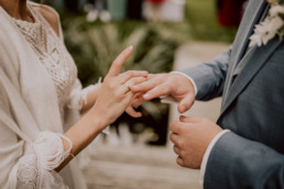Braut steckt Bräutigam den Ring an mit Anstecker von Ganz Unverblümt