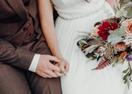 Braut und Bräutigam geben sich die Hand mit Strauß von Ganz Unverblümt in herbstlichen Farben