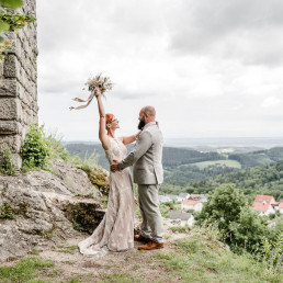 Braut und Bräutigam freuen sich vor Aussicht der Burg Brennberg