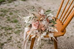 Boho Brautstrauß in arten Rosa Tönen liegt auf Stuhl