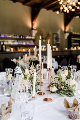Eingedeckter Tisch mit natürlichen Gestecken und kupfernen Kerzenständern von Ganz Unverblümt