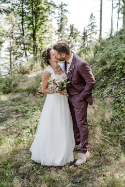 Braut und Bräutigam küssen sich im Wald mit Hochzeitsschmuck von Ganz Unverblümt Franzi
