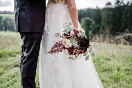 Braut und Bräutigam umarmen sich mit Brautstrauß von Ganz Unverblümt in Händen