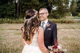 Bräutigam lächelt Braut an mit Haarkranz und Strauß von Ganz Unverblümt