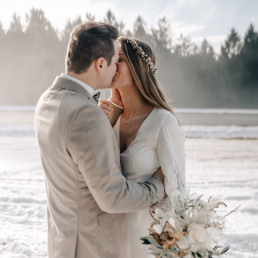 Braut und Bräutigam küssen sich mit winterlichem Brautstrauß von Ganz Unverblümt