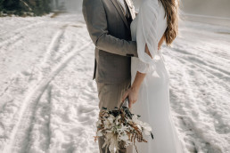 Braut und Bräutigam umarmen sich mit winterlichem Brautstrauß von Ganz Unverblümt
