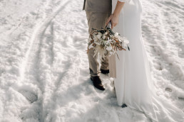 Braut und Bräutigam stehen im Schnee mit natürlichem Brautstrauß von Ganz Unverblümt Steinach
