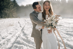 Braut und Bräutigam lachen glücklich mit natürlichem Brautstrauß von Ganz Unverblümt in der Hand