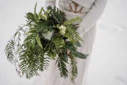 Braut hält komplett grünen Brautstrauß im Schnee in den Händen von Ganz Unverblümt