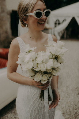 Braut lacht glücklich mit weißem Brautstrauß komplett aus Rosen von Ganz Unverblümt