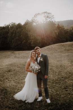 Braut und Bräutigam lachen glücklich mit Anstecker und natürlichem Brautstrauß von Ganz Unverblümt