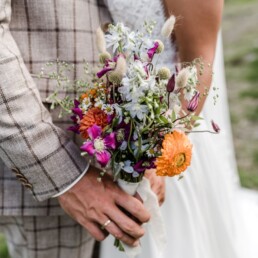 Braut und Bräutigam halten bunten Wiesenblumenstrauß von Ganz Unverblümt