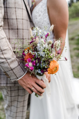 Braut und Bräutigam halten bunten Wiesenblumenstrauß von Ganz Unverblümt