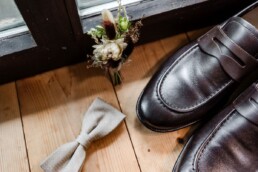 Anstecker, Schuhe und Fliege vom Bräutigam beim Getting Ready im Vierfalthof Geisenhausen